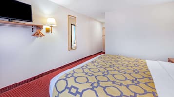 A hotel room with a bed, a TV mounted on the wall, a mirror, and a wall-mounted lamp.