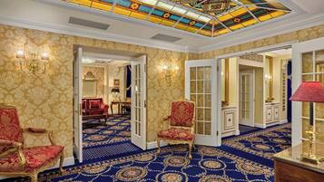 A grand room with a blue carpet, ornate chairs, and a stained glass ceiling.