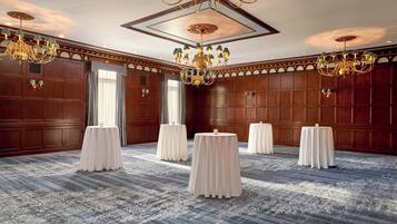 Une salle de conférence spacieuse, dotée d’un plafond haut, de lustres décoratifs et d’un tapis à motifs.