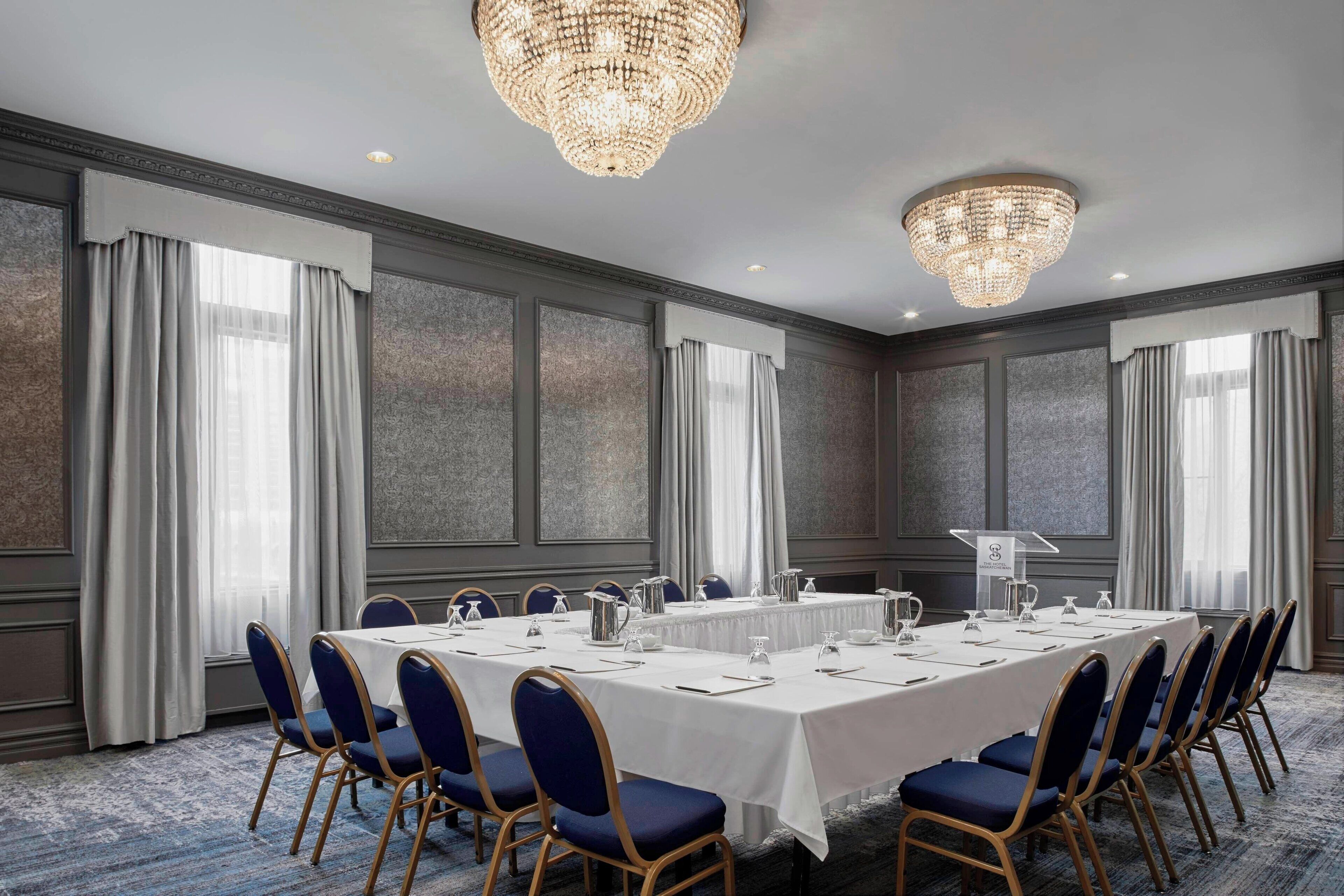 A conference room with a long table, blue chairs, and chandeliers.