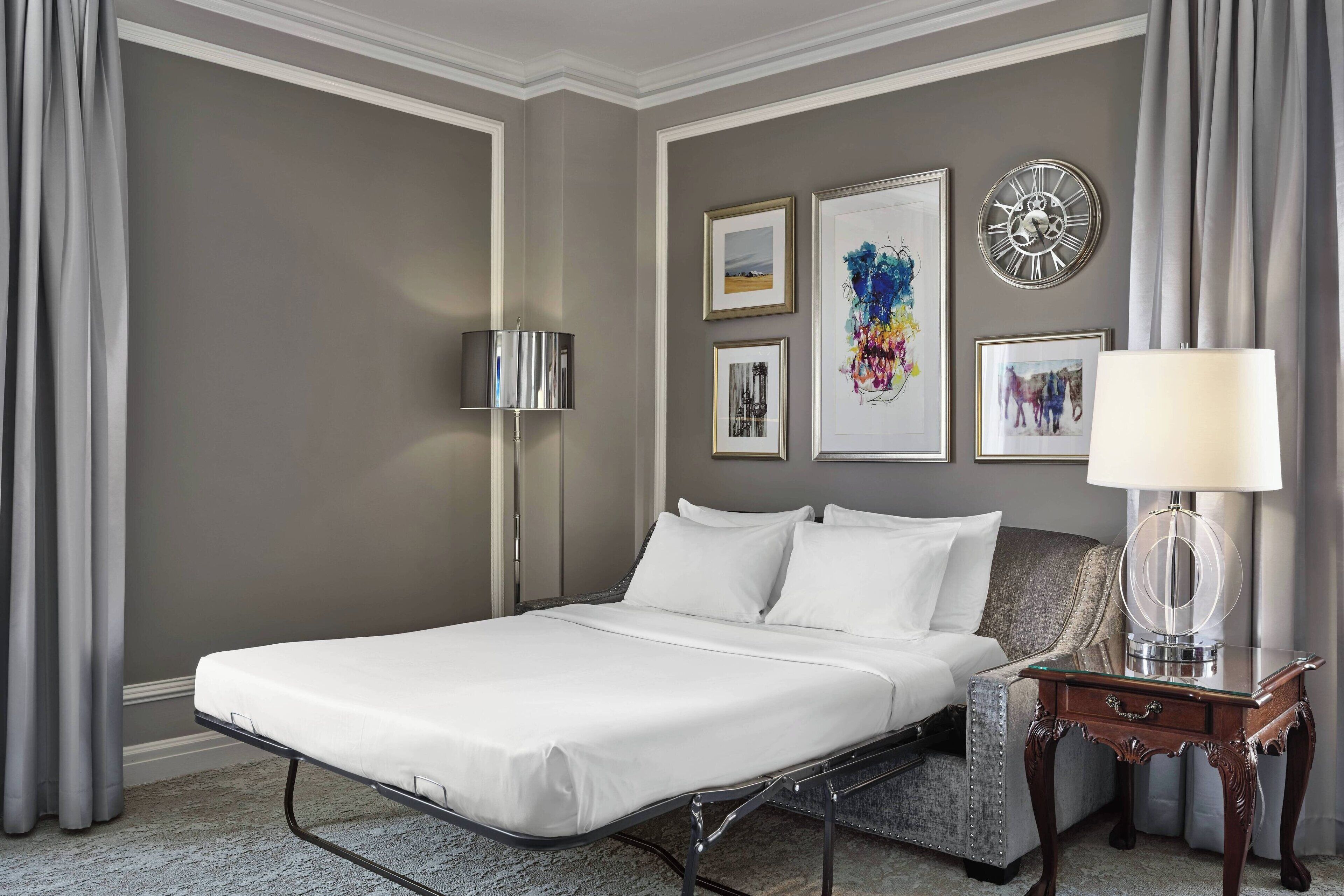 Une chambre d’hôtel avec un lit simple, une table de chevet avec une lampe et des œuvres d’art encadrées accrochées au mur.