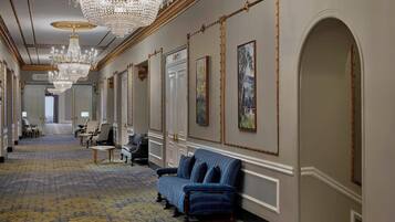 A grand hallway with chandeliers, a blue sofa, and framed artwork on the walls.