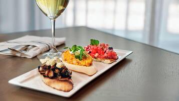 Un plato con tres tipos diferentes de aperitivos y una copa de vino blanco sobre una mesa de madera.