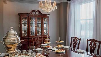 Uma sala de jantar formal com uma mesa de vidro, talheres, louça e um suporte de três andares com doces.