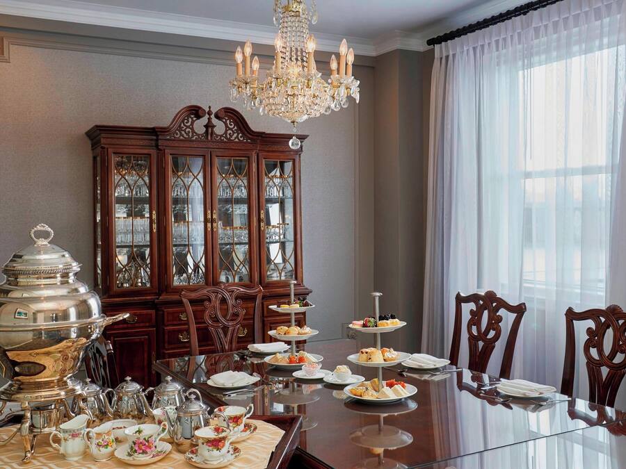 Uma sala de jantar formal com uma mesa de vidro, talheres, louça e um suporte de três andares com doces.