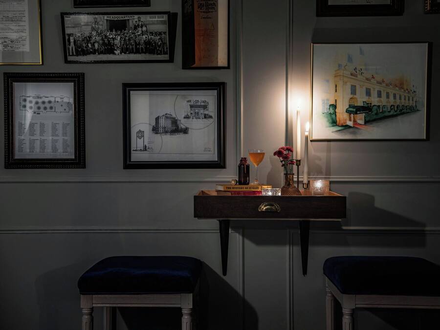 A dimly lit room with framed photographs on the wall, a desk with a candle, and two upholstered chairs.