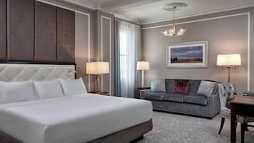 Una habitación de hotel con una cama grande, un sofá gris, un escritorio y una araña.
