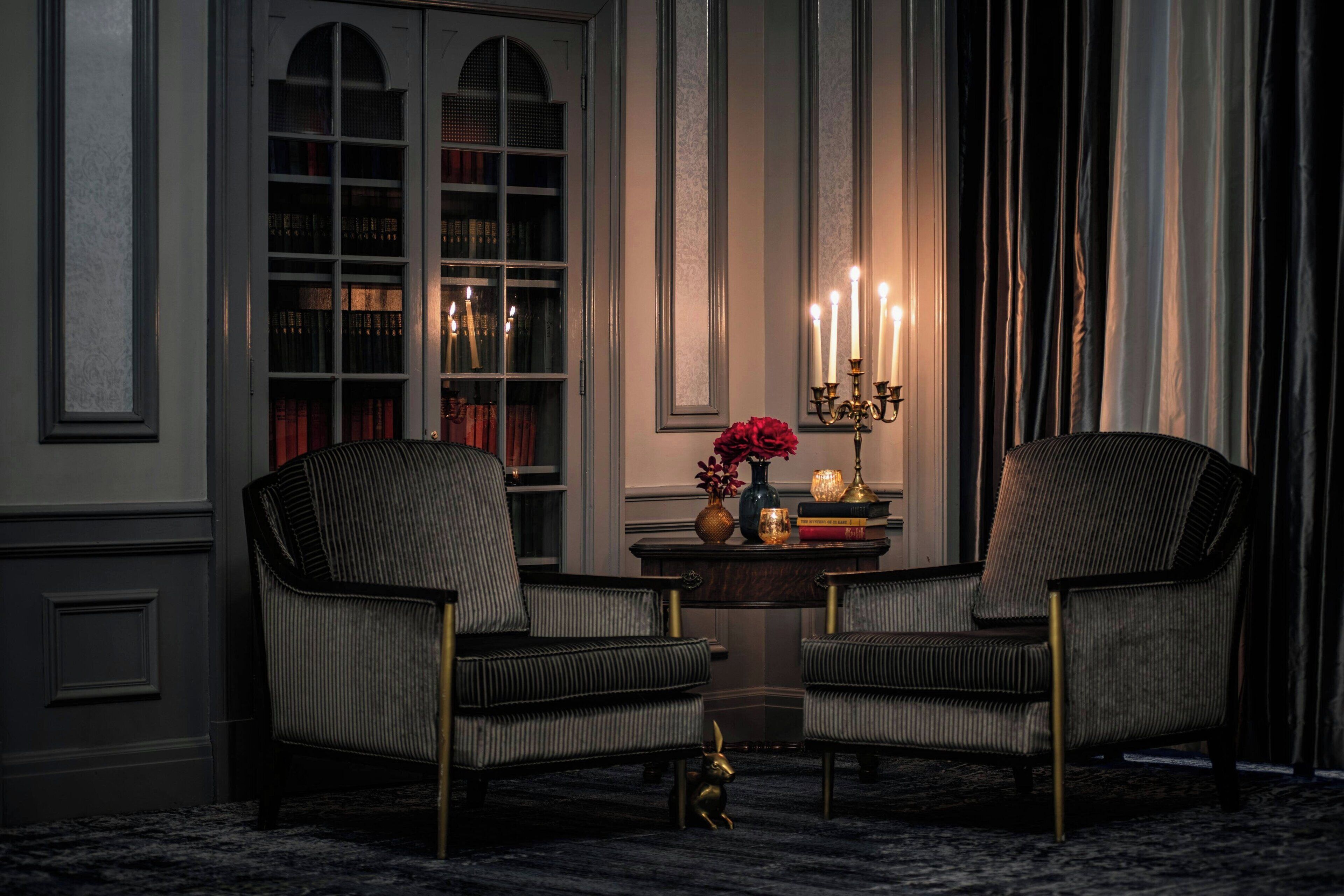 Una habitación con dos sillones tapizados, una mesita con un florero y libros, y un candelabro con velas encendidas.