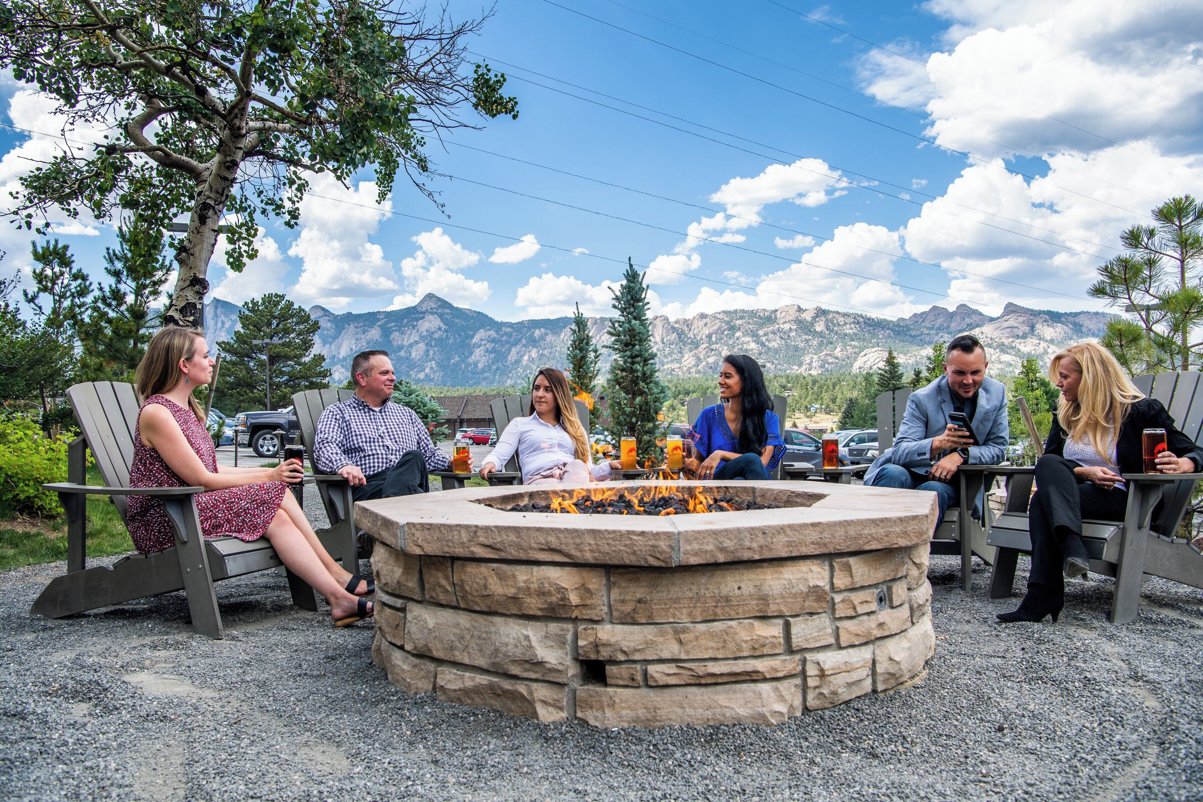 A group of people seated around a stone fire pit with a mountainous backdrop.