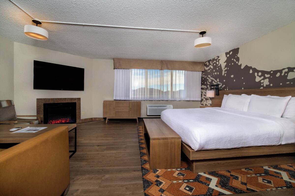 Una habitación de hotel moderna con una cama grande, un televisor de pantalla plana, una chimenea, un escritorio y una alfombra estampada.