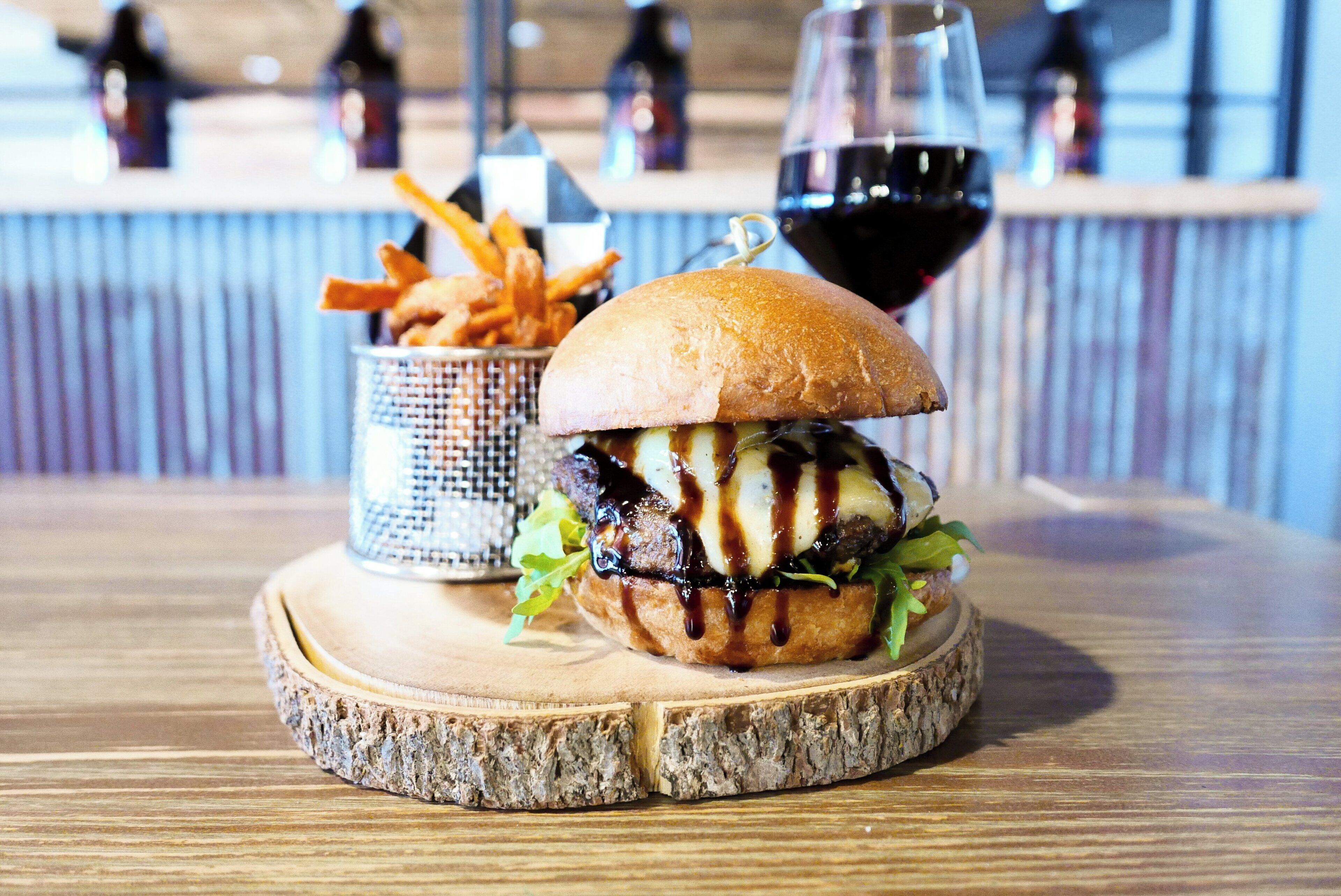 Ein Burger mit Pommes und einem Glas Rotwein auf einem Holzteller.