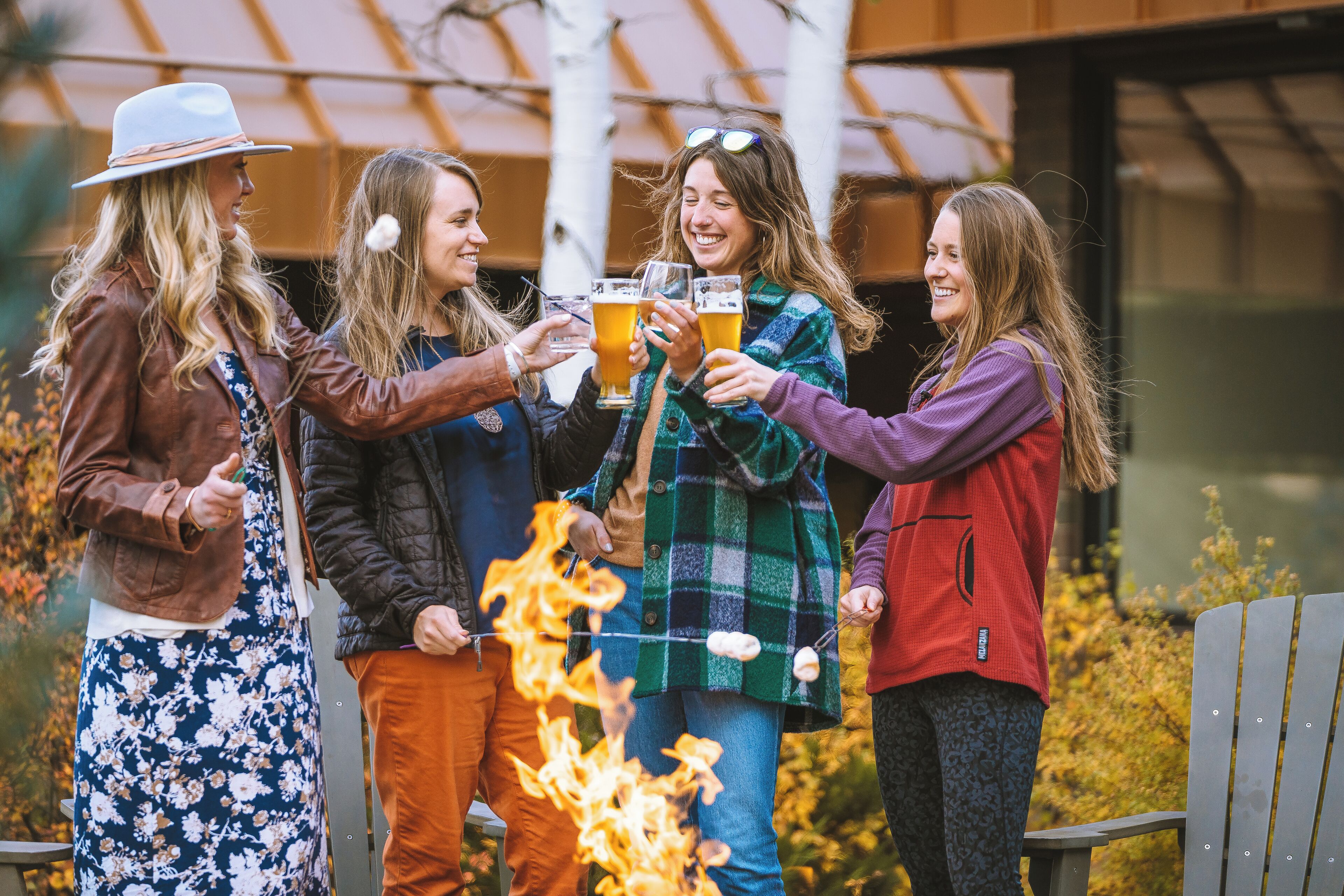 Een groep mensen proost met bierglazen rond een kampvuur.