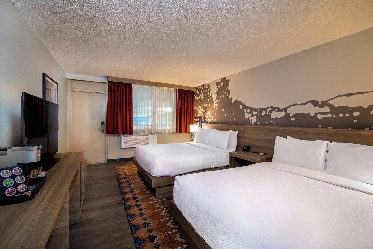 Habitación de hotel con dos camas, televisión, escritorio con cafetera y un mural en la pared.