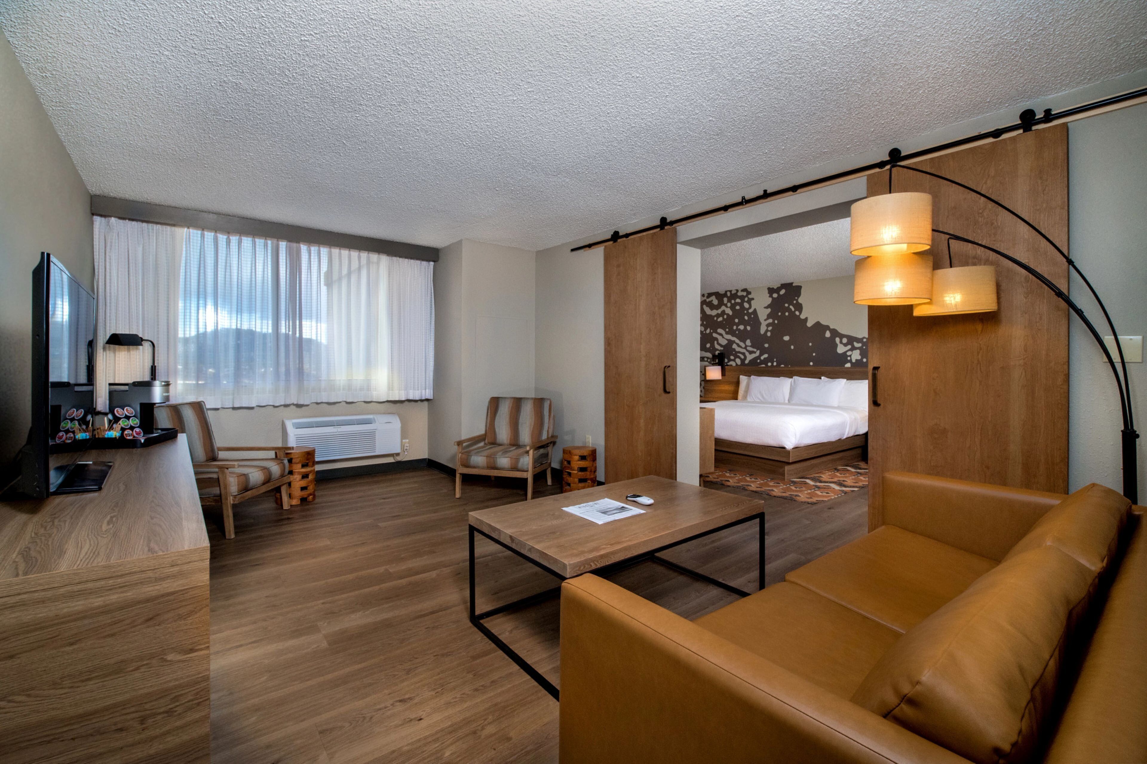 A hotel room with a bed, a sofa, a coffee table, a desk with a lamp, and a chair.