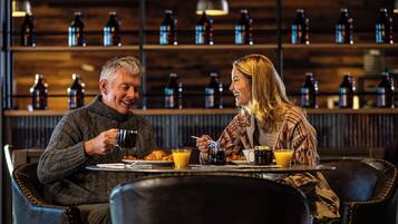 Two people sitting at a table with breakfast items, in a room with shelves of bottles in the background.