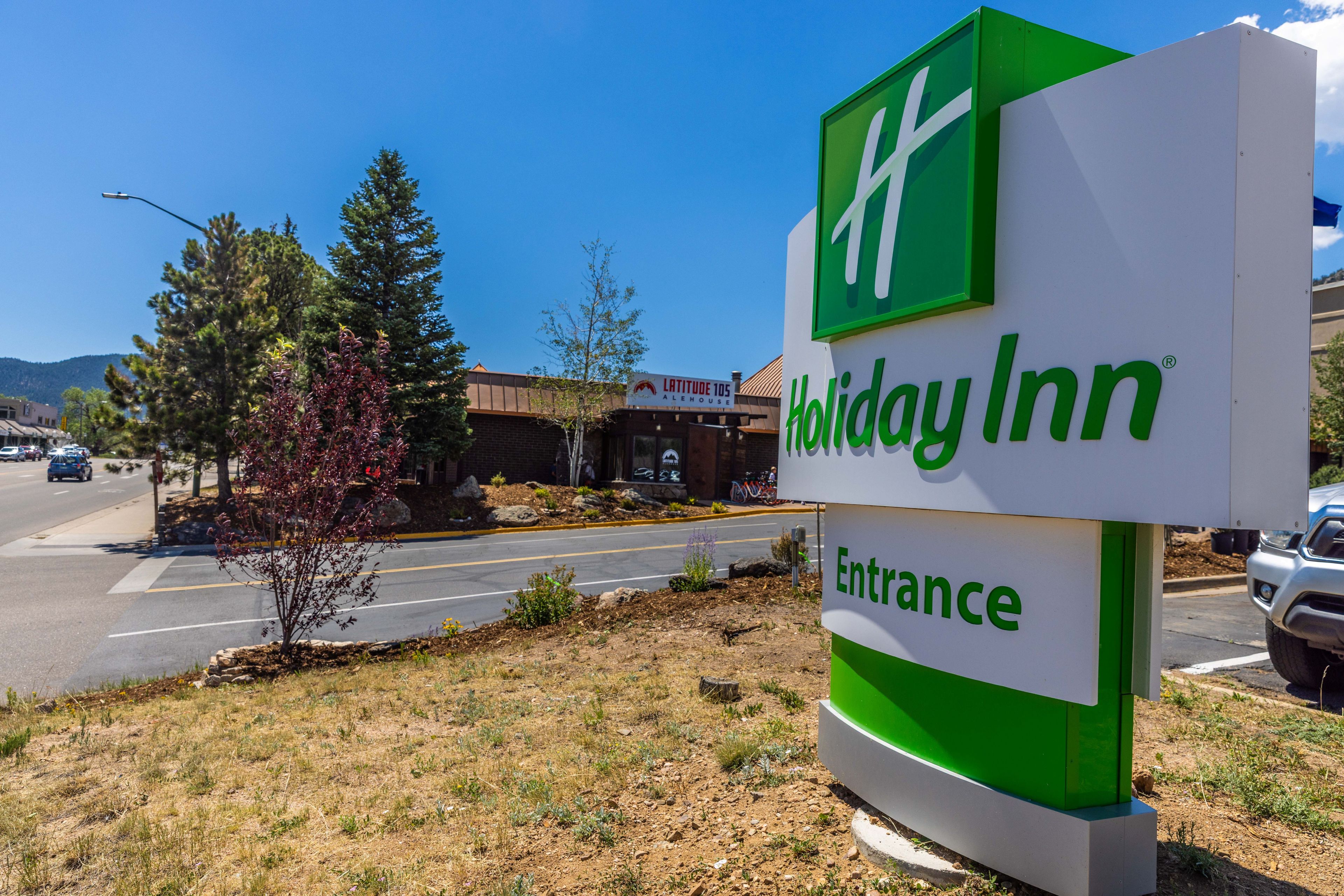 A Holiday Inn entrance sign with a clear view of the surrounding area including a road, a building labeled 'Latitude 105', and some trees.