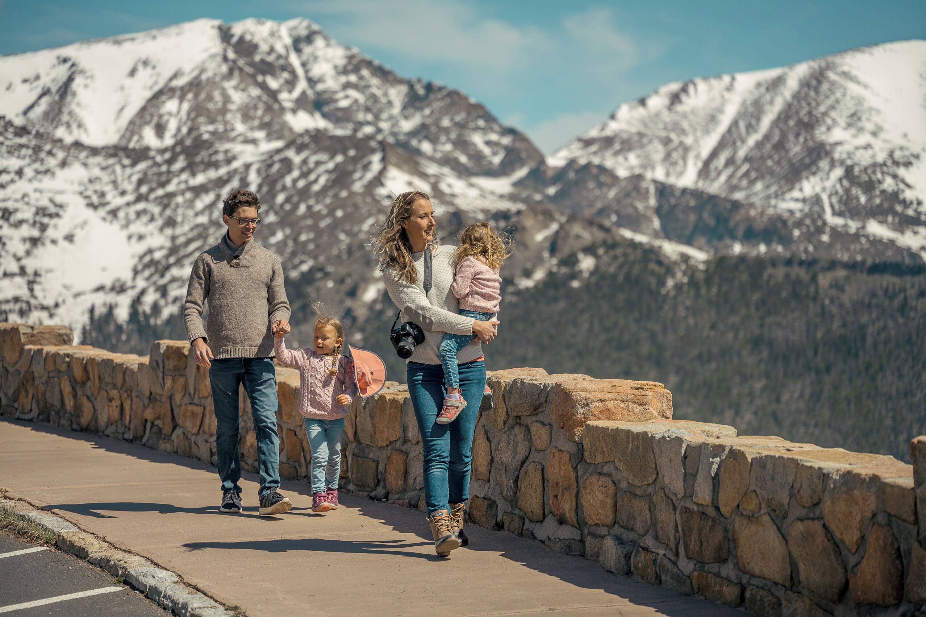 Eine Familie geht auf einem steinernen Weg entlang, im Hintergrund schneebedeckte Berge.