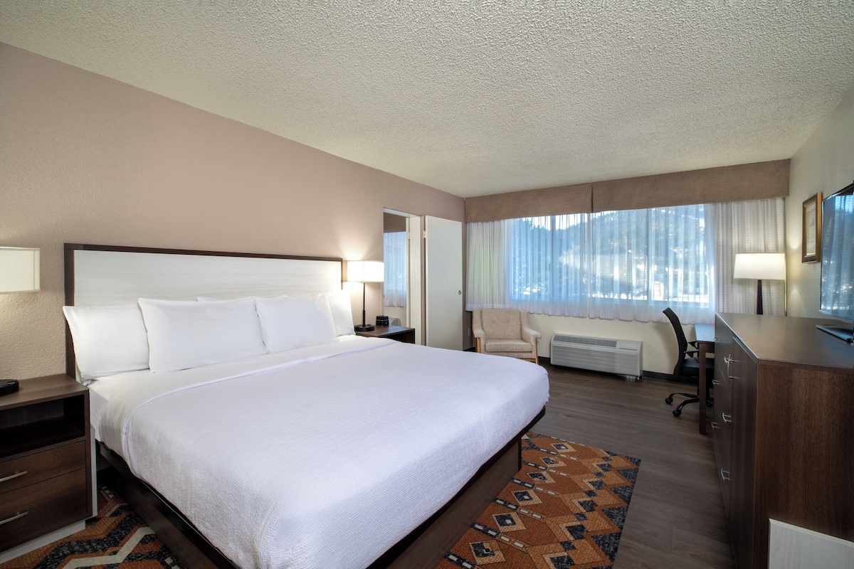 Une chambre d’hôtel avec un grand lit, un bureau, une chaise et une lampe de bureau.