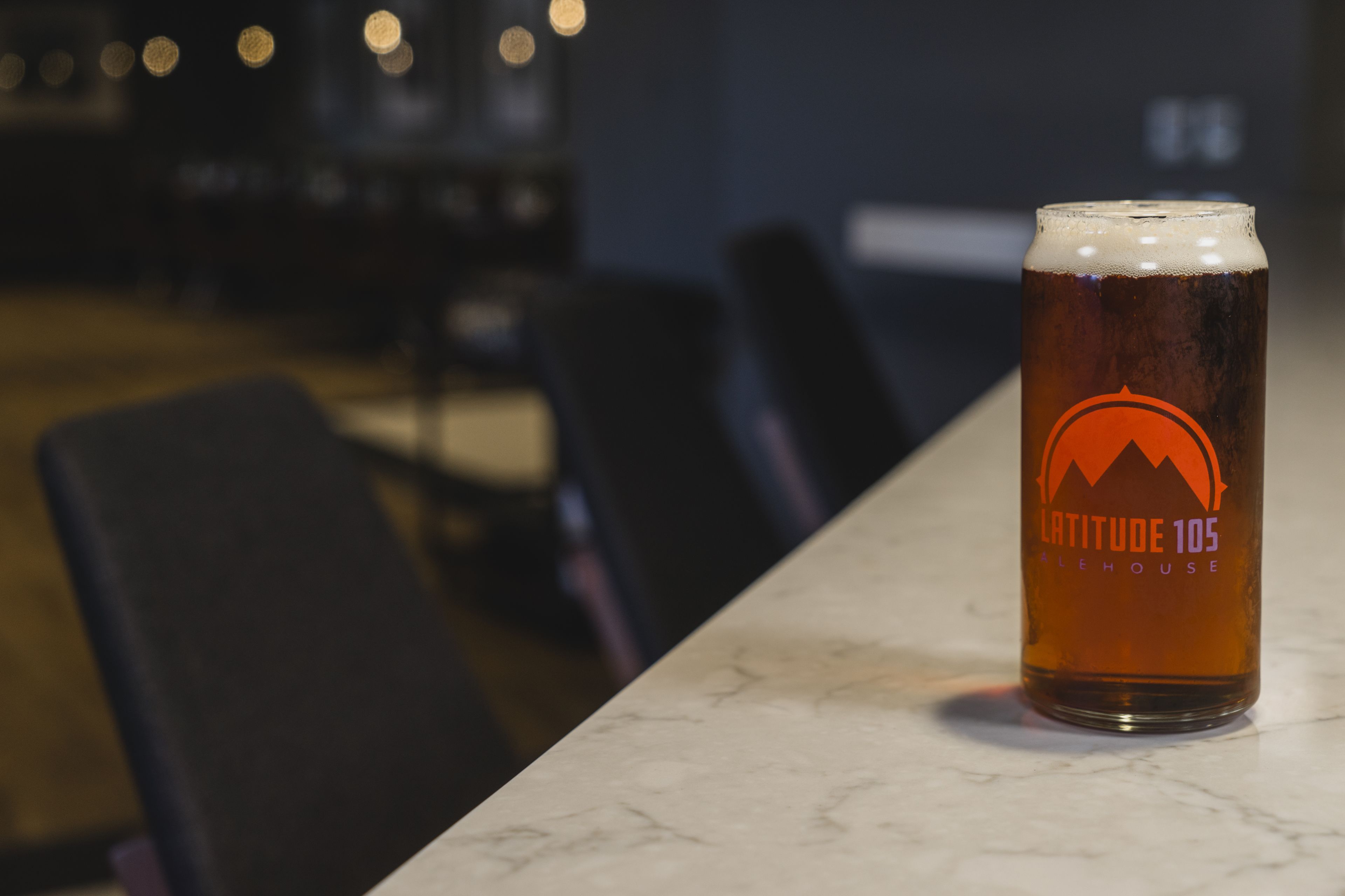 Un got de cervesa amb un logotip sobre un taulell de marbre en una habitació poc il·luminada amb cadires.