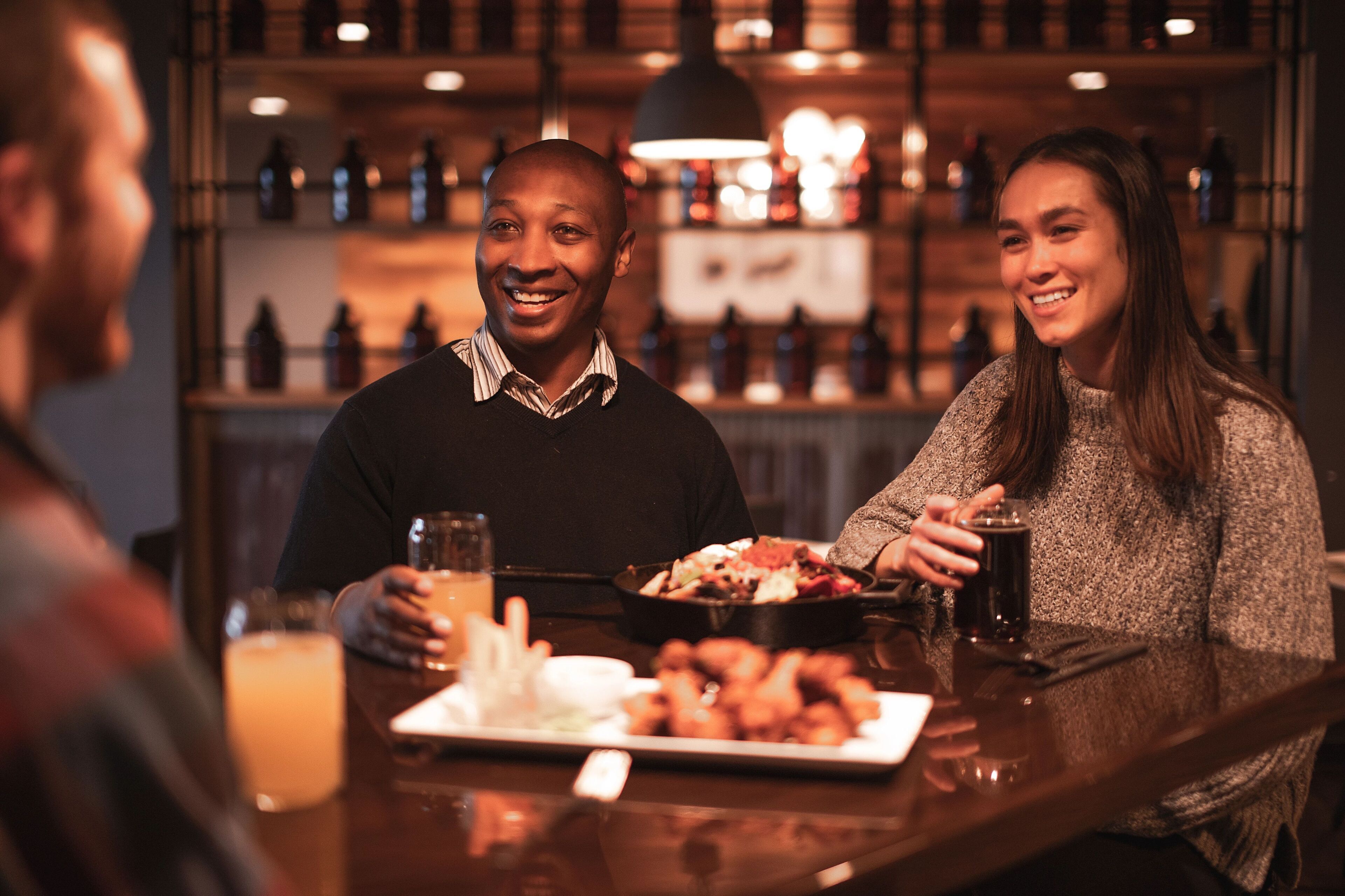 A bar setting with a person holding a drink and another person with a plate of food.