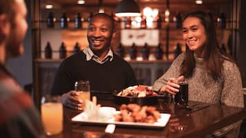 A bar setting with a person holding a drink and another person with a plate of food.