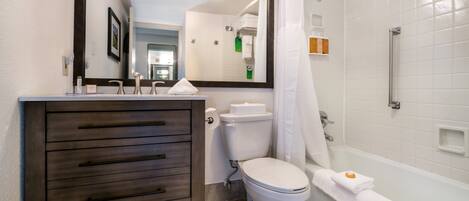 A bathroom with a wooden vanity, white toilet, and a bathtub with a shower curtain.