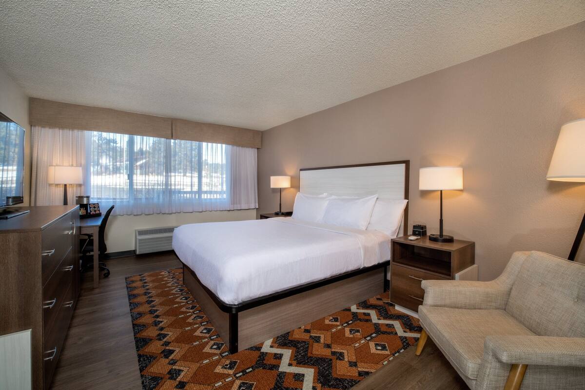 Habitación de hotel con cama, escritorio, silla y ventana con cortinas.