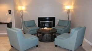 A room with four light blue armchairs around a central coffee table, a fireplace, and two floor lamps.
