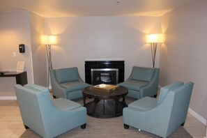 Um quarto com quatro poltronas azul-claras dispostas ao redor de uma mesa de centro, uma lareira e duas luminárias de chão.