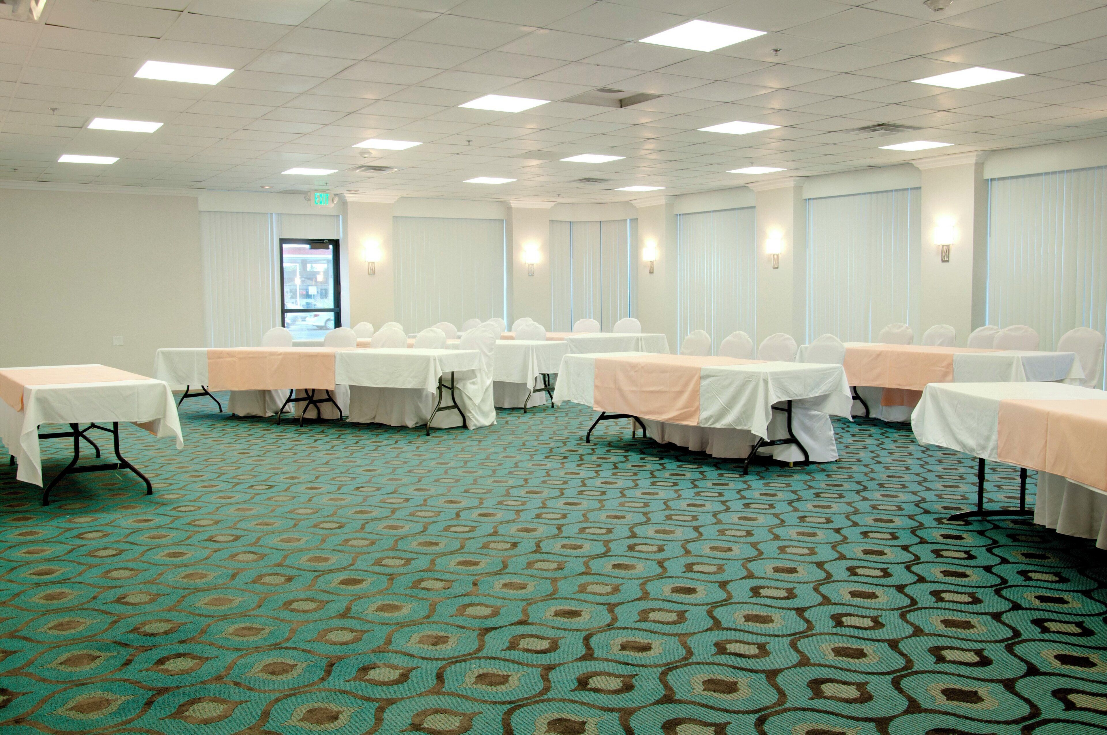 A conference room with multiple tables, chairs, and a patterned carpet.