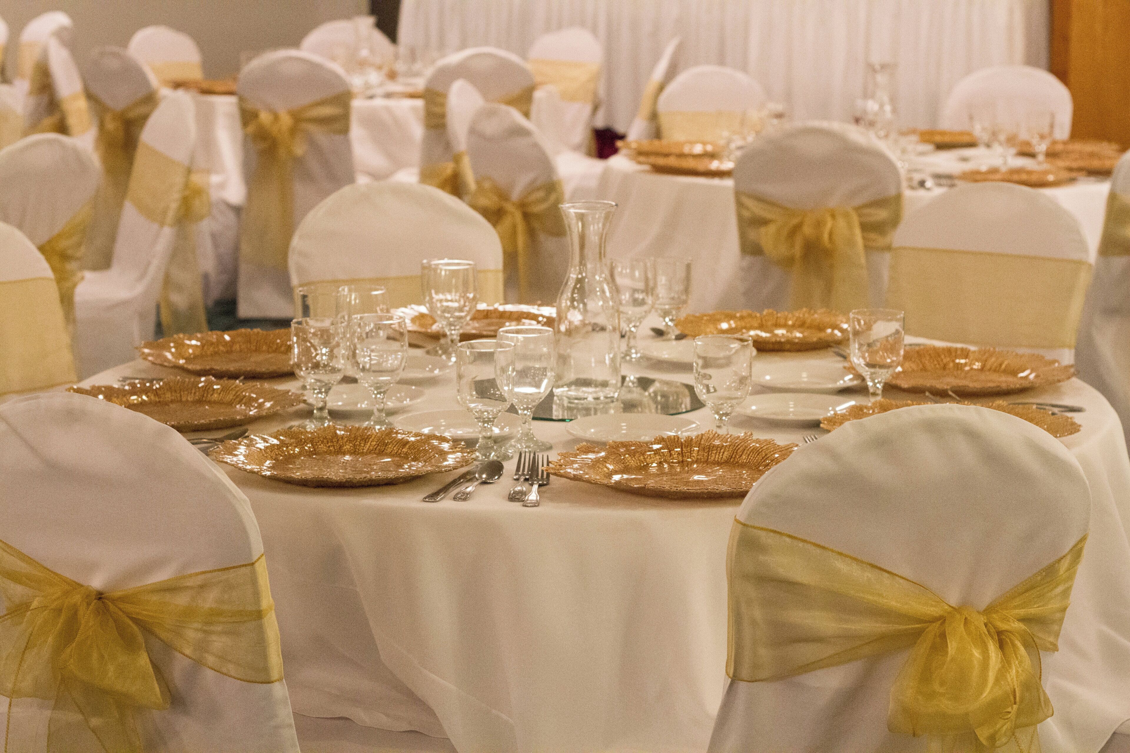 Een lange tafel gedekt met witte tafelkleden, borden met gouden rand en helder glaswerk.