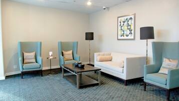 A modern hotel room with a sofa, two armchairs, a coffee table, a floor lamp, and a wall-mounted picture.