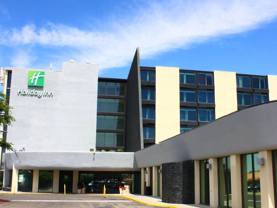 Un hotel Holiday Inn con diseño moderno, que presenta un logotipo verde destacado, ventanas amplias y un estacionamiento.