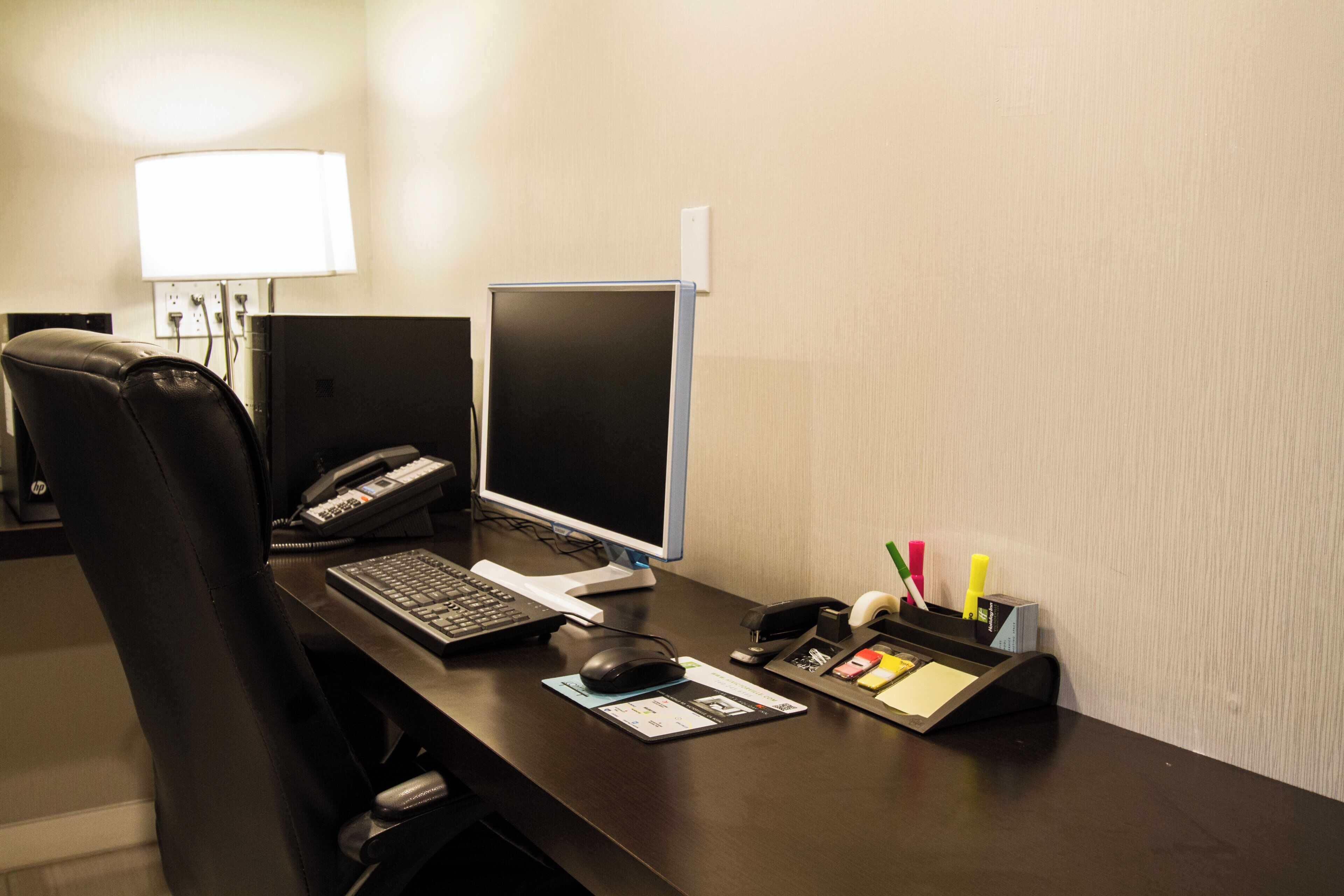 Balcão de atendimento de hotel com computador, teclado, rato, telefone e diversos materiais de escritório.