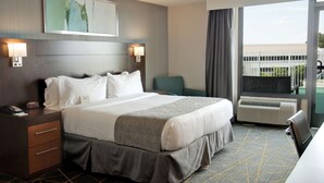 A hotel room with a large bed, bedside lamps, a desk with a phone, and a view of the outside through a large window.