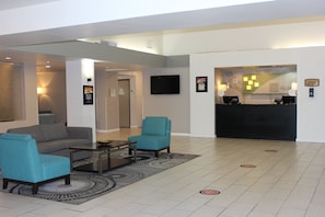 A modern lobby with a sofa, armchairs, a coffee table, a reception desk, and a flat-screen TV. - Holiday Inn Victorville by IHG (Victorville)