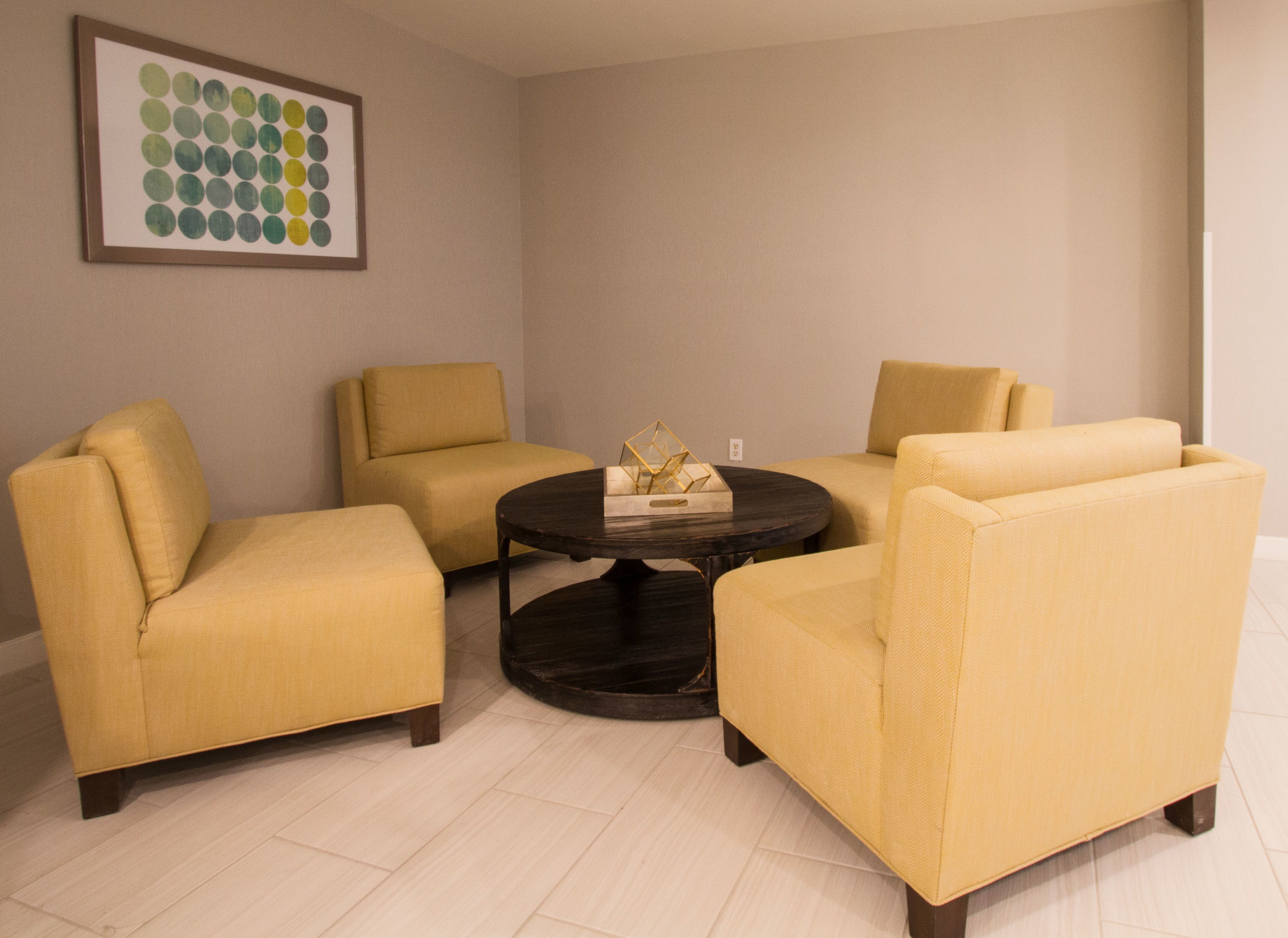 Una habitación con cuatro sillones amarillos dispuestos alrededor de una mesa de centro redonda oscura.