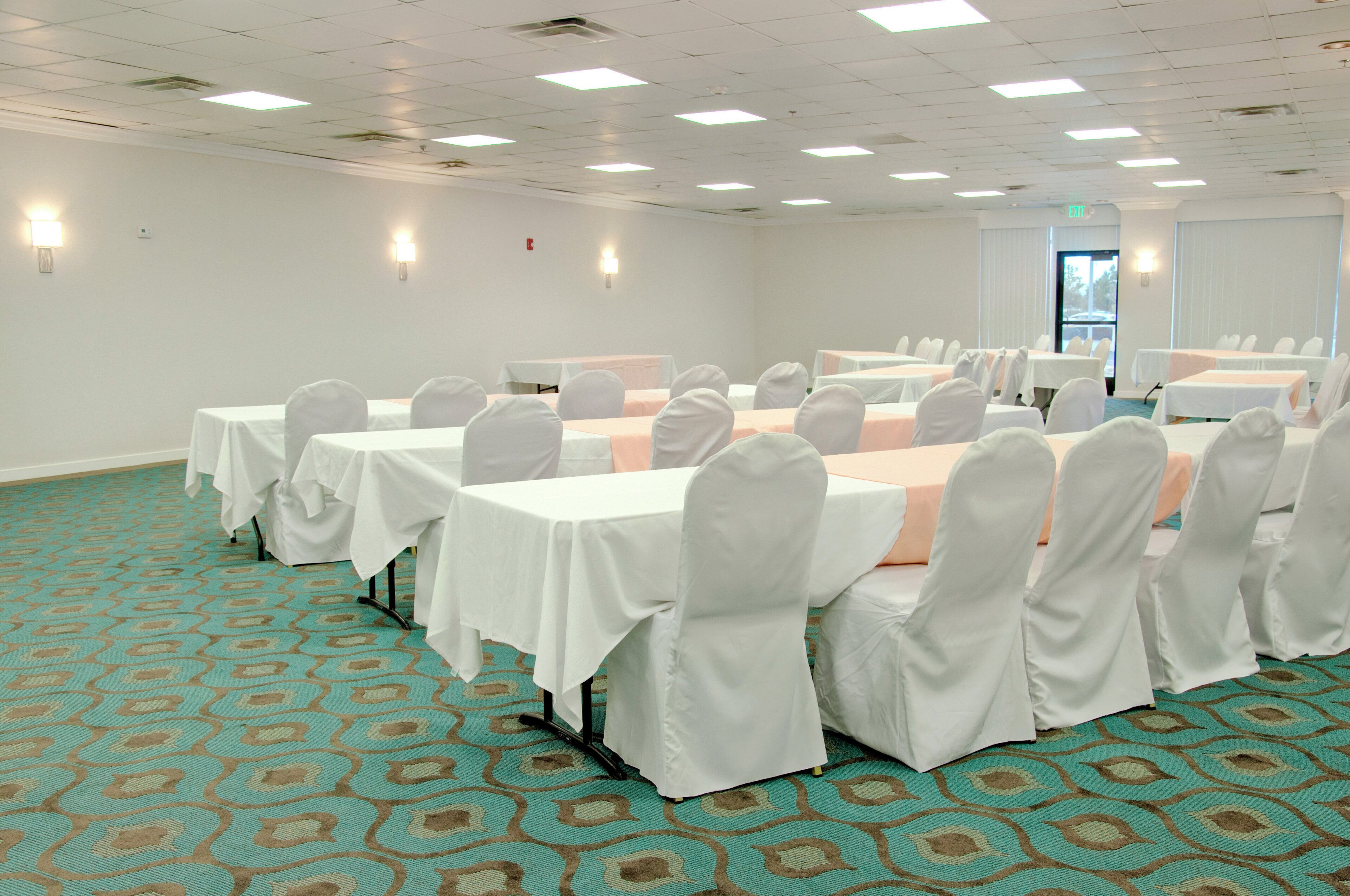 Un salón de conferencias con mesas y sillas, piso alfombrado e iluminación en el techo.