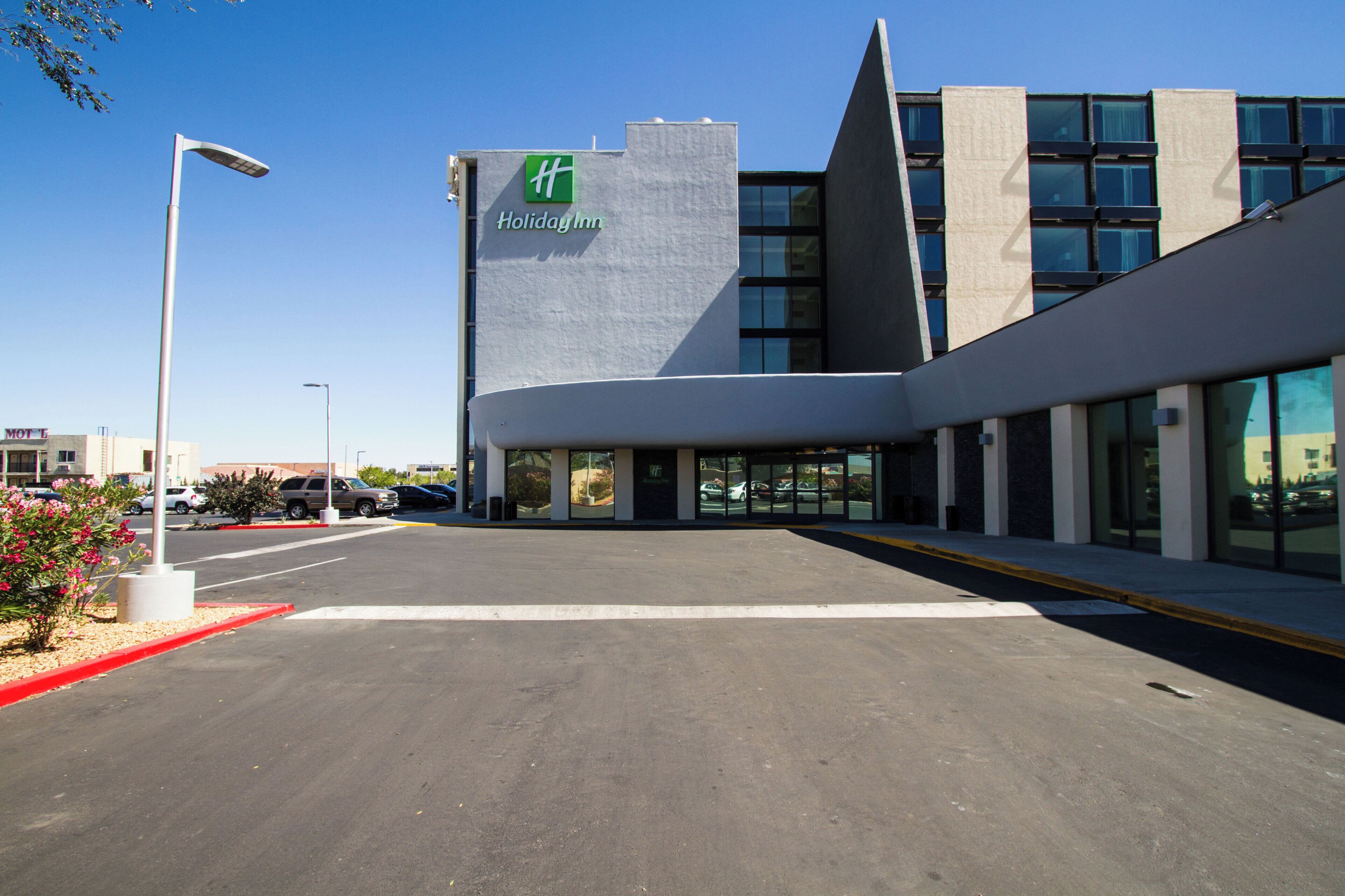 Un edificio moderno con un llamativo letrero de 'Holiday Inn', un estacionamiento y cielo despejado.