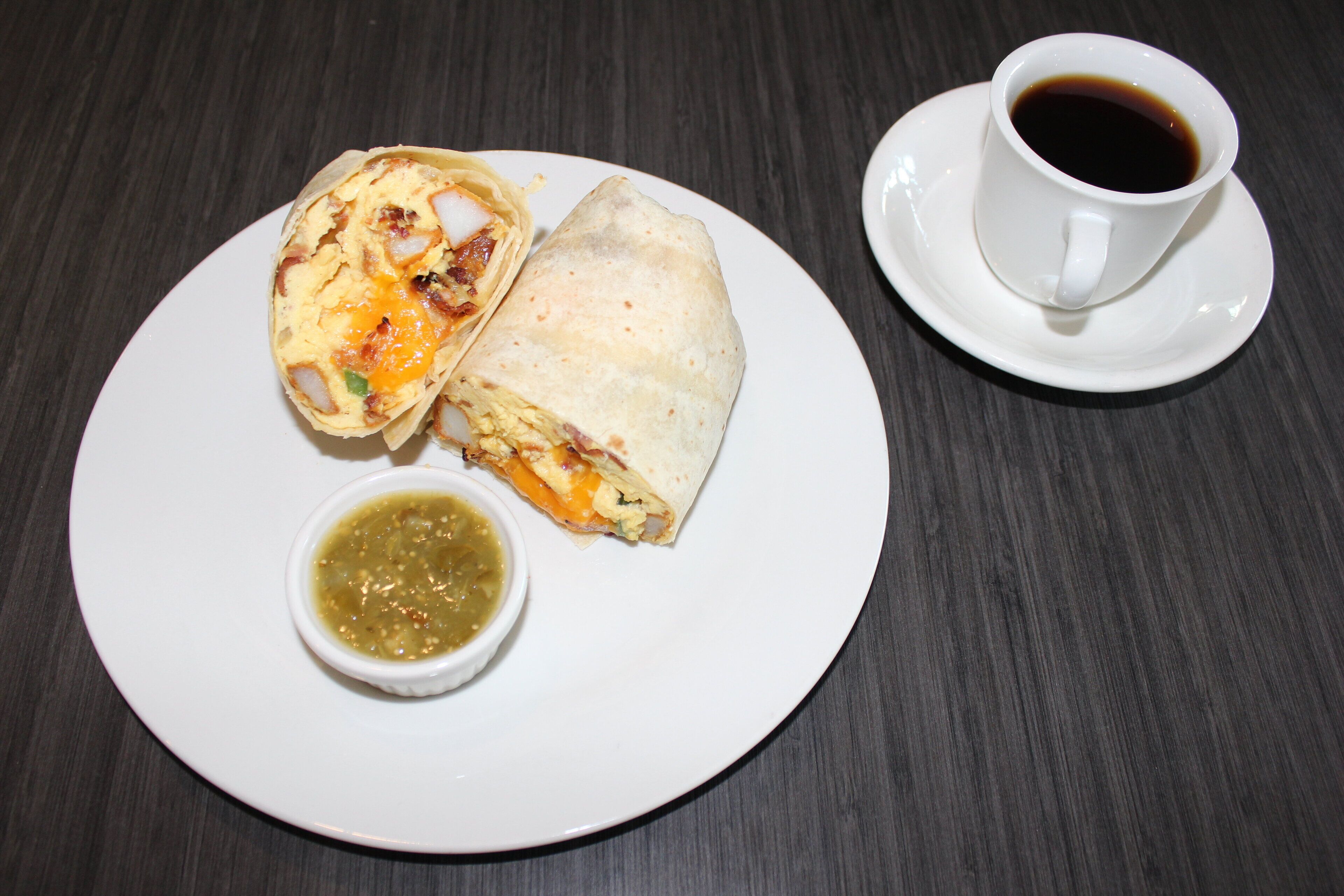 A plate with a burrito, a cup of coffee, and a small bowl of salsa.