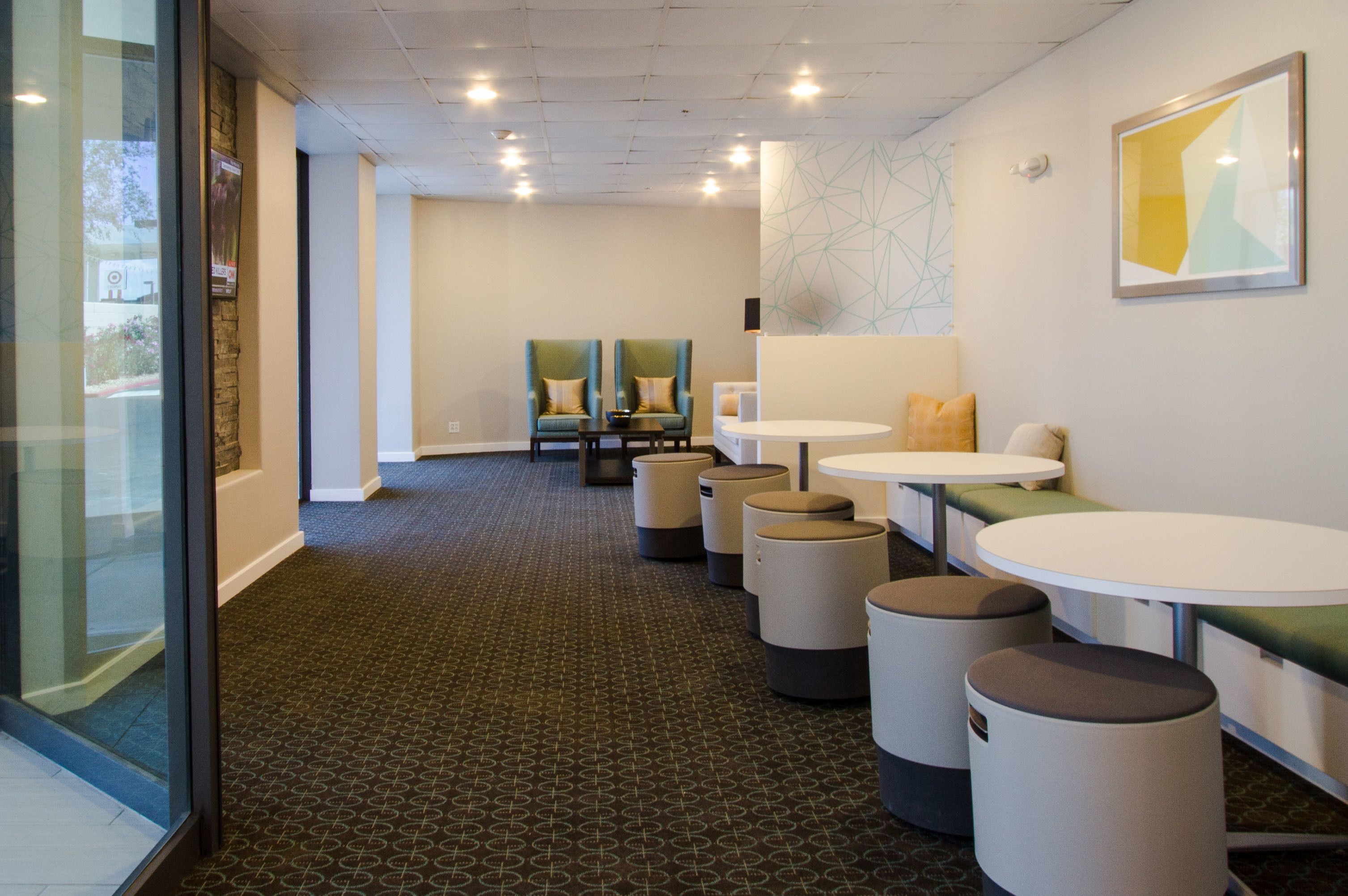 Een moderne hotellobby met een patroonrijk tapijt, zithoeken met stoelen en tafels, en een glazen wand aan de zijkant.
