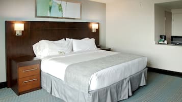 A hotel room with a large bed, a wooden nightstand with drawers, a wall-mounted lamp, and a painting above the bed.