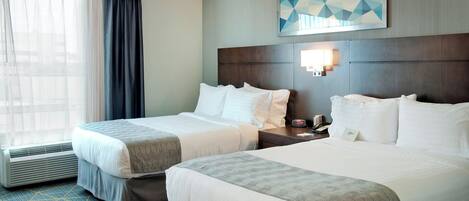 A hotel room with two beds, a large window with curtains, a wall-mounted artwork, and a nightstand with a phone and clock.