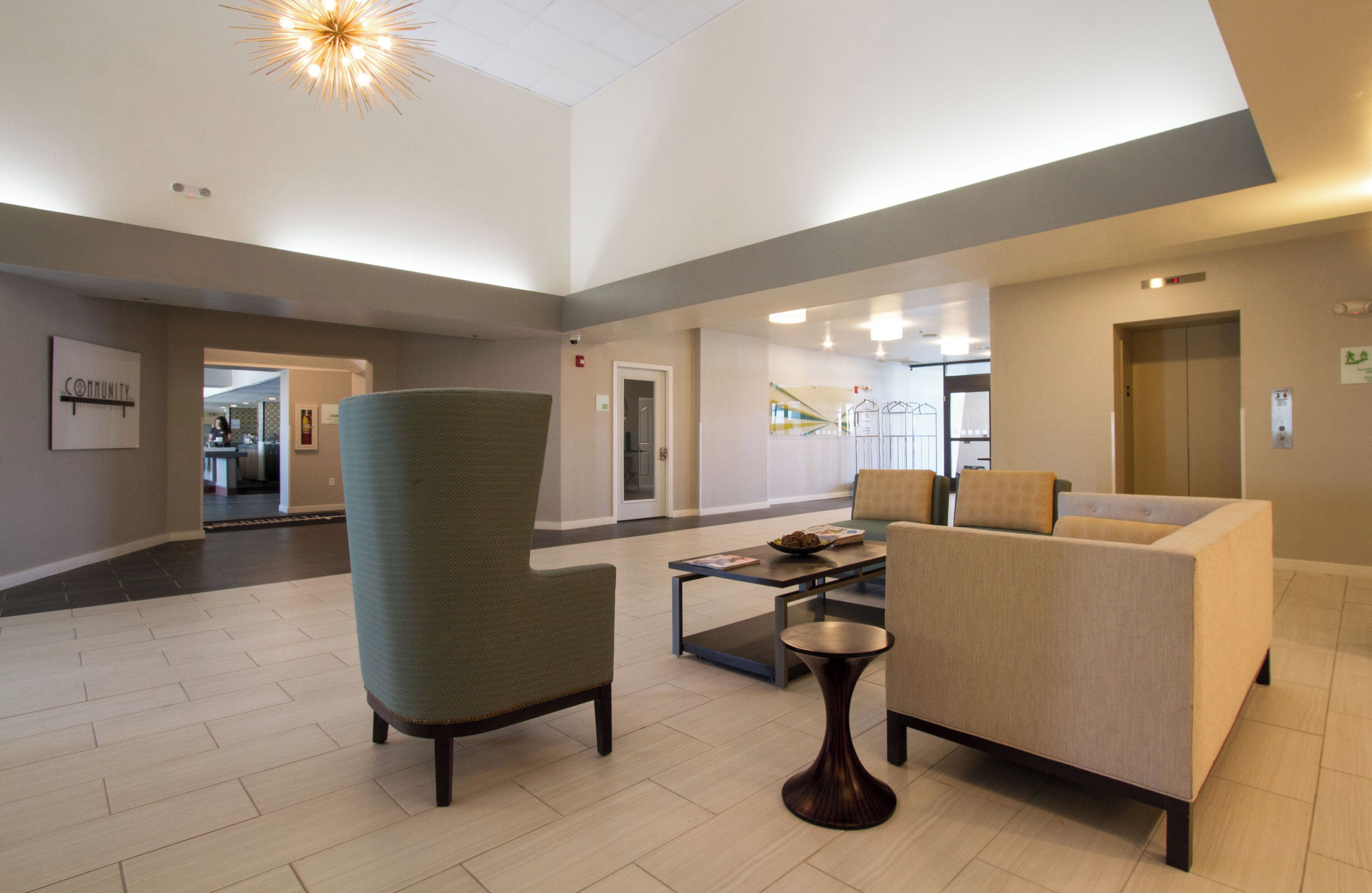 A lobby with a high ceiling, a green armchair, a beige sofa, and a small table with magazines.