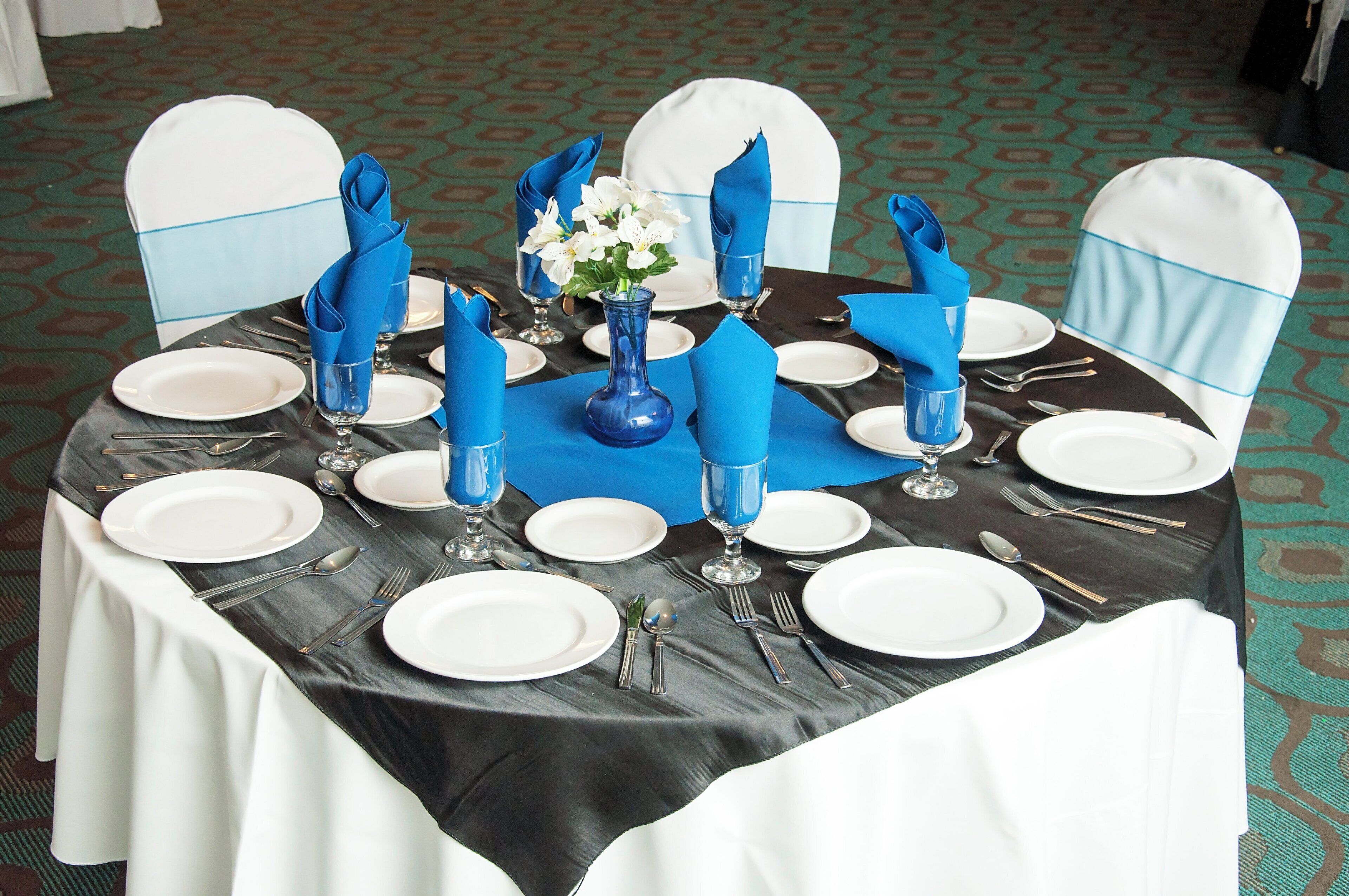 A table set for six with white plates, silverware, and blue napkins.