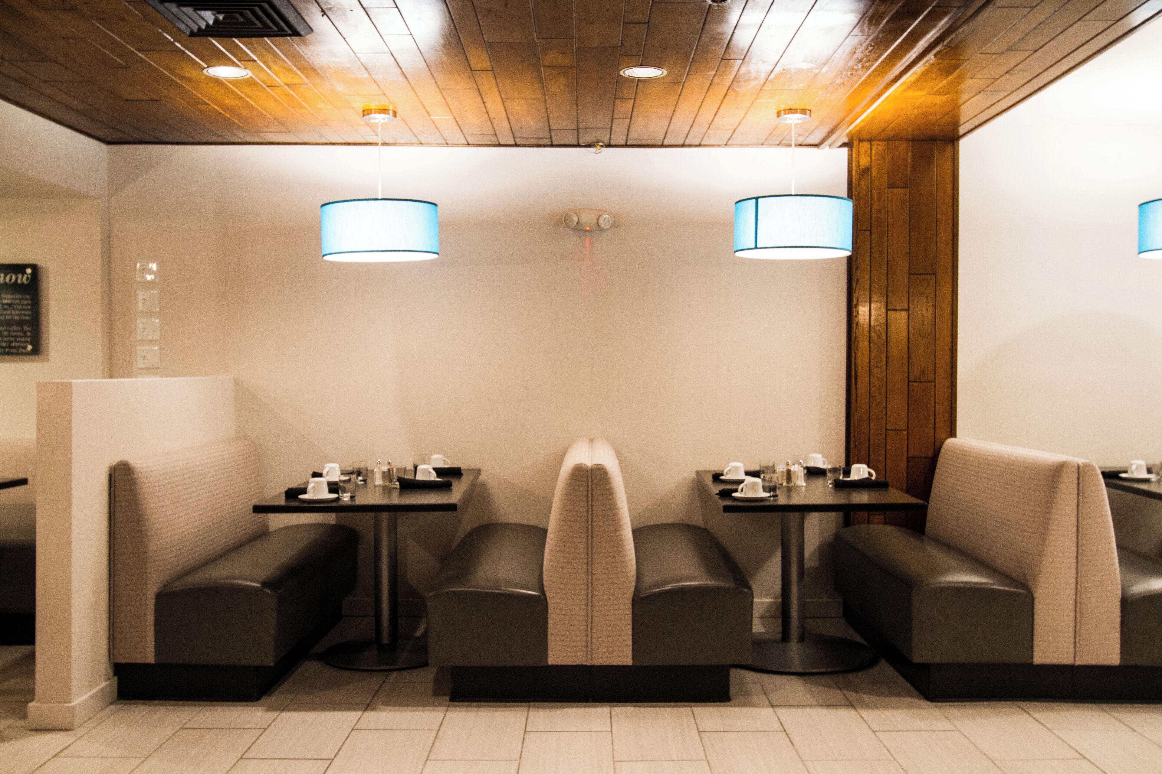 A restaurant interior with booth seating and tables, wooden ceiling, and pendant lighting.