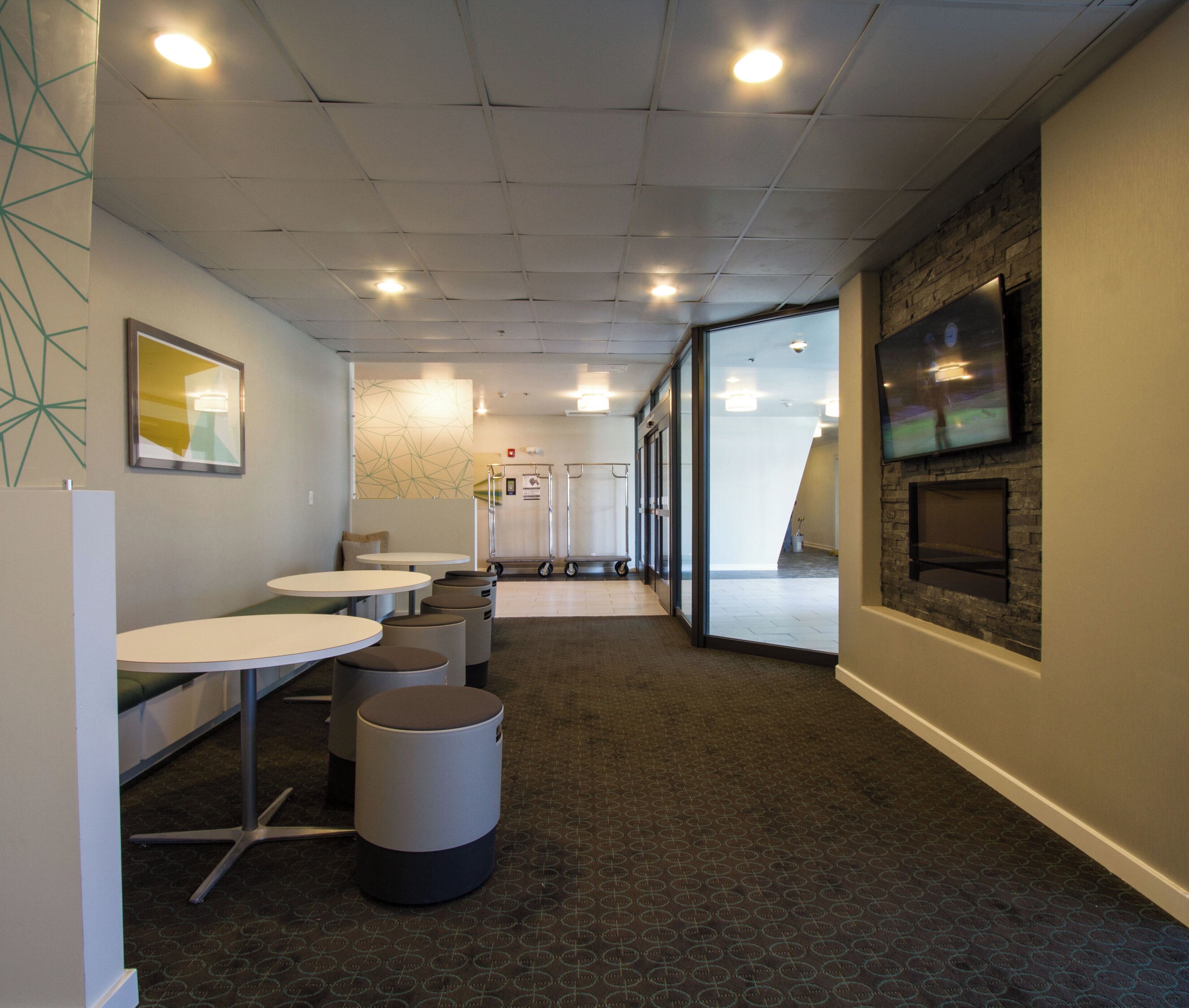 A modern interior with round tables and trash bins, a TV on the wall, and a patterned carpet.