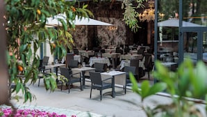 Un restaurante al aire libre con mesas y sillas, rodeado de follaje y flores.