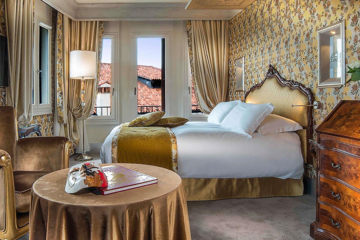 A hotel room with a bed, a dresser, a round table with a book, and a chair.