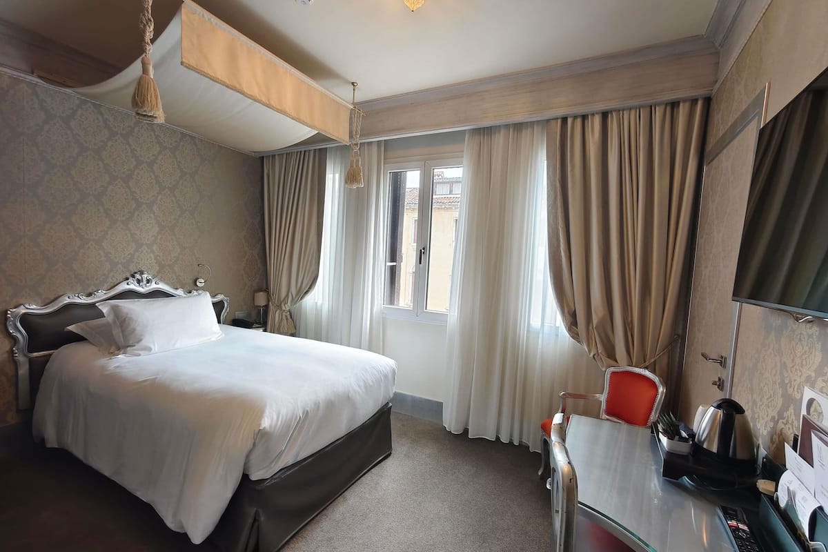 A hotel room with a bed, a desk, a chair, a TV, and a window with curtains.